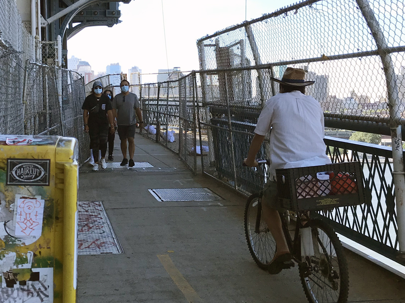 The
                Manhattan Bridge's pedestrian space with many cyclists
                riding through it